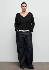 Čierny sveter s výstrihom do „V“, voľný strih, kombinovaný so širokými tmavomodrými džínsami. Jednoduchý dizajn, hladká textúra a jemné švy.