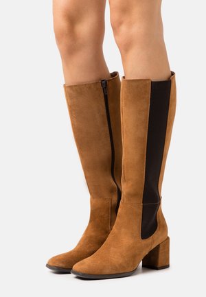 Stivali alti fino al ginocchio in suede color cammello con pannelli laterali elastici e una zip nera. Tacco a blocco spesso, punta liscia e parte superiore texturizzata.