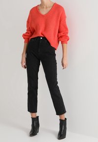 Maglione in maglia color corallo con scollo a V, abbinato a jeans neri a vita alta e taglio corto. Completa il look con stivaletti neri dalla finitura sfrangiata.