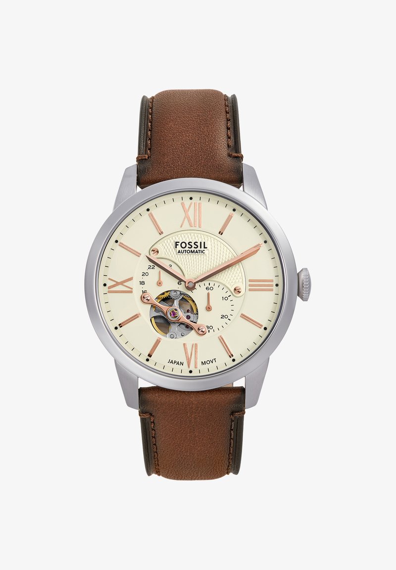 Montre automatique Fossil avec cadran crème, chiffres romains en or rose, mécanisme d'engrenage visible et bracelet en cuir marron.