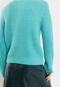 Suéter de punto color turquesa con textura acanalada, con mangas largas y dobladillo recto, combinado con una falda de cuero negra.