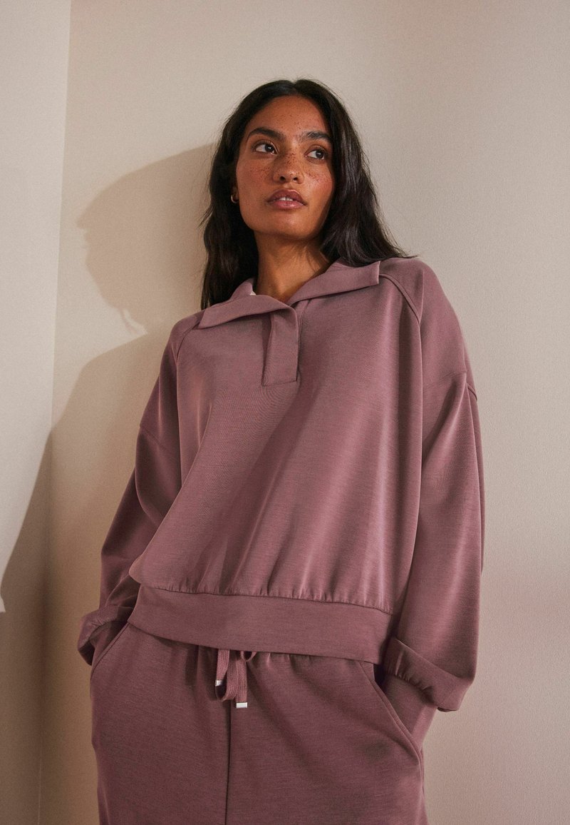 Pullover oversize in mauve tenue, con colletto piatto, spalle cadenti, polsini a coste e orlo con cordini. Tessuto morbido e liscio.