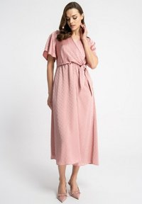 Jasnoróżowa sukienka maxi z krótkimi rękawami, w fasonie kopertowym, z wiązaniem w talii i fakturowanymi kropkami. Połączona z dopasowanymi różowymi szpilkami w szpic.