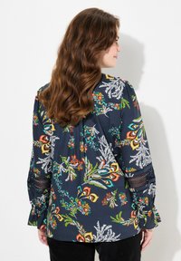 Blusa floreale blu navy con maniche lunghe, caratterizzata da vivaci stampe multicolori, delicati dettagli in pizzo sulle maniche e una vestibilità comoda.