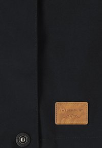 Schwarzer Stoff mit einem aufgenähten braunen Lederpatch, geprägt mit "SWEDEMOUNT" und einem Berglogo, sowie einem schwarzen Knopf darunter.