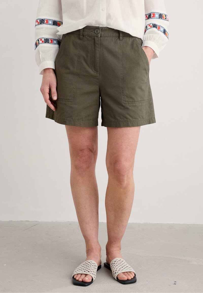 Olivgröna shorts tillverkade av bomullsblandning, med en rak framsida, två sidofickor och knappstängning. Pairade med vävda sandaler.