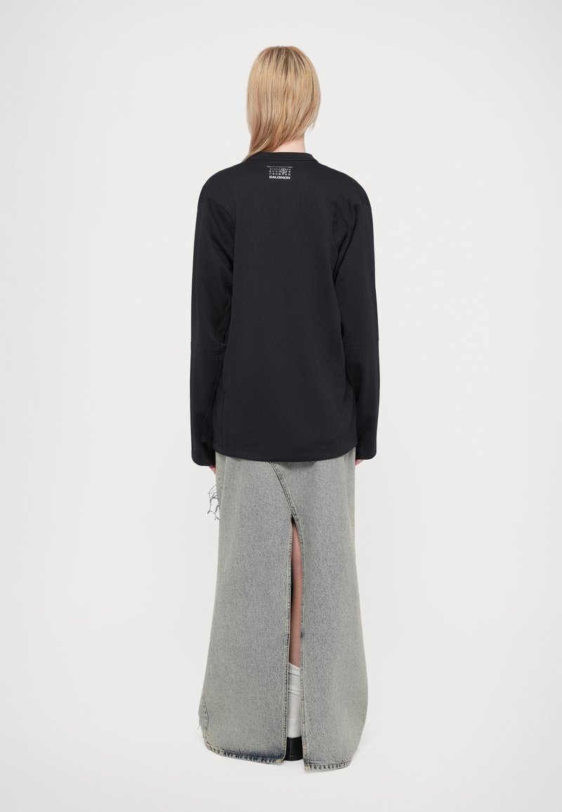 Sort langærmet top med tekstureret design og rund hals, parret med en lys grå denimbundkjole med en frontslids og slidte detaljer.