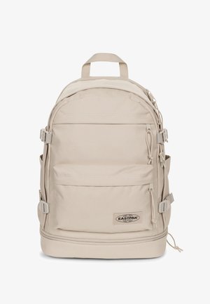 Mochila Eastpak beige con forma redondeada, correas ajustables, múltiples bolsillos y un parche de marca. Fabricada con un tejido duradero de textura suave.