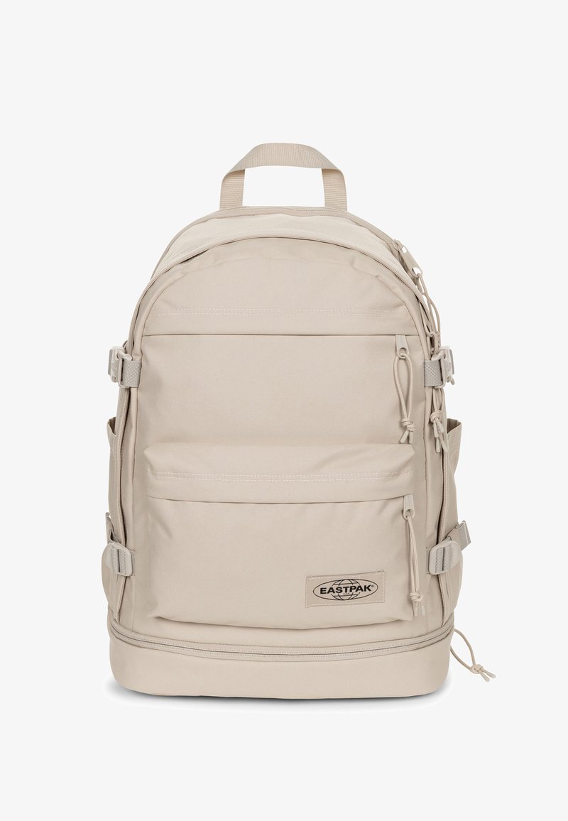 Zaino Eastpak beige dalla forma arrotondata, con spallacci regolabili, numerose tasche e una patella con il marchio. Realizzato in tessuto resistente con una superficie liscia.