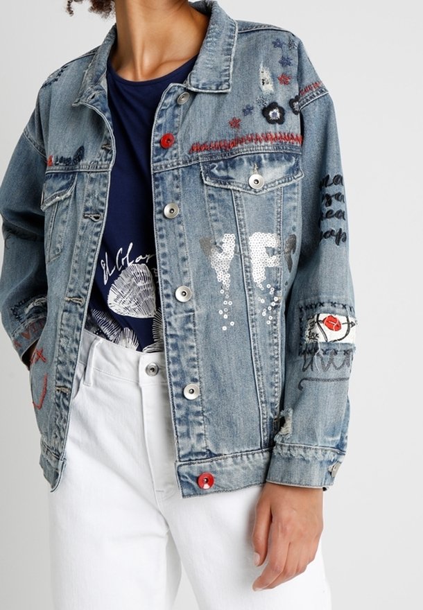 Džínová bunda s vyšívanými květinovými a abstraktními vzory, červenými a bílými knoflíky, nošená přes námořnické tričko s potiskem a bílé kalhoty.