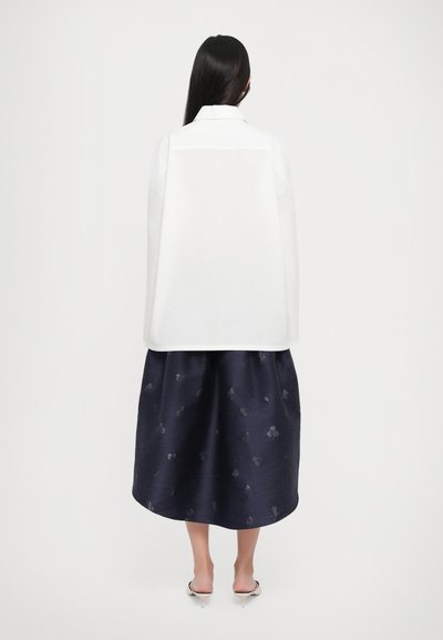 White collared shirt with long sleeves paired with a knee-length navy skirt featuring a subtle floral pattern. Smooth fabric texture, minimalist design.