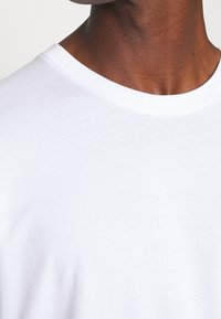 Camiseta blanca con cuello redondo, hecha de suave tela de algodón, que presenta una textura lisa y un diseño minimalista sin patrones.