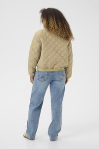 Jachetă bej matlasată cu o croială lejeră, cu manșete și tiv ribbrate, purtată cu blugi de denim bleu deschis, cu o croială clasică și buzunare la spate.
