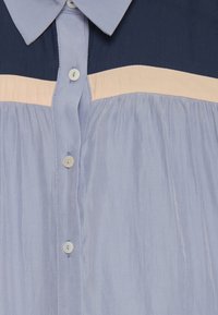 Jasnoniebieska koszula z guzikami, z granatową górną częścią, brzoskwiniowym poziomym pasem oraz fakturowanym materiałem z lekko marszczoną talią.