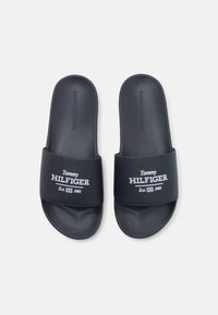 Sötétkék csúszó szandál sima szintetikus felsőrésszel, fehér hímzett "Tommy HILFIGER" logóval és "Est. 1985" részlettel.