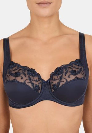 Woman wearing a navy blue bra with floral lace embroidery on sheer mesh upper cups and solid fabric lower cups.