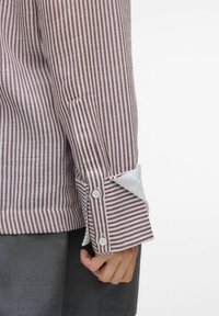 Chemise à rayures avec des rayures étroites bordeaux et blanches, doublure des poignets blanche et poignets classiques. Le tissu est lisse avec une finition nette.