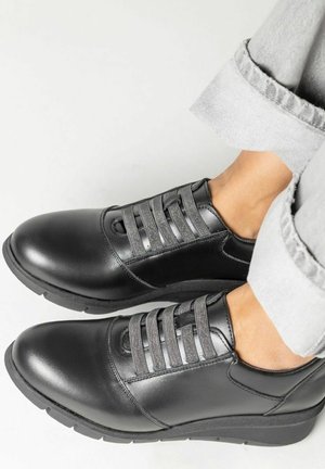 Zapatos de cuero negro con cordones elásticos, puntera redondeada y detalle texturizado en la parte superior. Cuentan con una suela de goma gruesa para un buen agarre y comodidad.