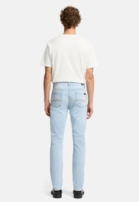 Jasnoniebieskie dżinsy o dopasowanym kroju z tylnymi kieszeniami, które mają żółte przeszycia. Noszone z prostą białą koszulką i czarnymi butami.