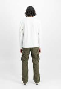 Witte langzijdige shirt gecombineerd met olijfgroene cargo broek met zijzakken, relaxte pasvorm en opgerolde zoom. Minimalistisch ontwerp.