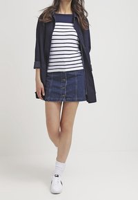 Denim mini kjol med knappstängning fram, kombinerad med en marinblå randig skjorta och en svart lätt jacka. Vita sneakers och strumpor fulländar looken.