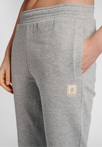 Grå joggingbukser med elastik i taljen, sidelommer og et stofmærke på hoften. Blød tekstur og afslappet pasform.