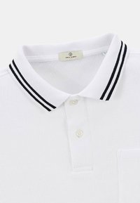 Polo shirt blanc en tissu texturé, avec un col rayé noir et blanc, trois boutons et une poche sur la poitrine gauche.