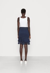 Falda azul marino con lunares, con un dobladillo con volantes y cintura elástica, combinada con una camiseta blanca sin mangas y zapatillas blancas.