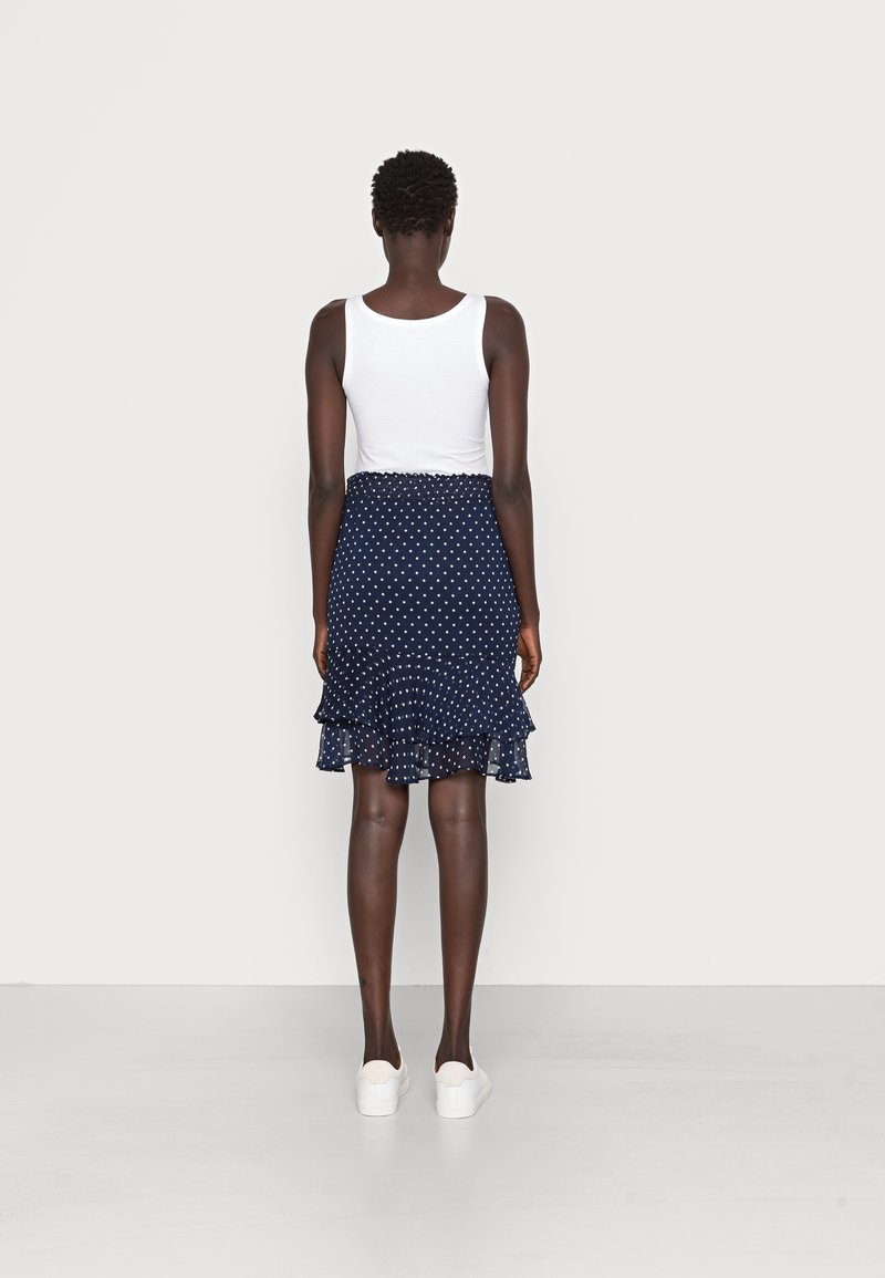 Falda azul marino con lunares, con un dobladillo con volantes y cintura elástica, combinada con una camiseta blanca sin mangas y zapatillas blancas.