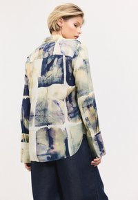 Multicolored button-up shirt featuring a watercolor pattern of squares in blue, cream, and tan. Made of lightweight fabric with a curved hem.