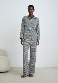 Woman standing barefoot on carpet wearing matching black and white geometric patterned long-sleeve shirt and wide-leg pants.