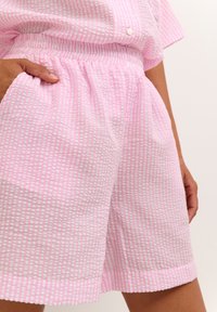 Shorts roses en tissu texturé, avec un motif de petites rayures blanches, dotés d'une taille élastique et de poches latérales.