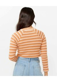Stribet crop top i orange og creme, med lange ærmer og en ribbet tekstur. Kombineret med lyseblå højhåndede jeans.