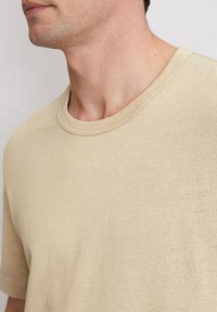 Beige T-Shirt mit kurzen Ärmeln und Rundhalsausschnitt, mit glatter Textur und tailliertem Schnitt. Keine sichtbaren Muster oder Akzente.