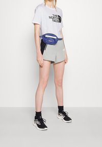 Šedé sportovní kraťasy s černými akcenty, světle fialové tričko s grafikou a modrá ledvinka. Černé tenisky s bílou podrážkou.