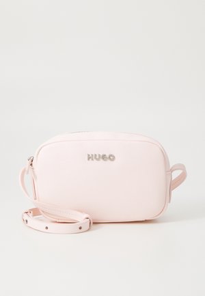 Jasnoróżowa torebka na ramię Hugo z srebrnym logo, regulowanym paskiem i zamkiem na górze na białym tle.