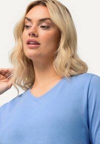 Světle modré tričko s výstřihem do V vyrobené z hladké tkaniny, s krátkými rukávy a volným střihem. Minimalistické švy a žádné viditelné loga.