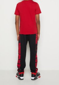 Červené bavlněné tričko s krátkým rukávem doplněné černými tepláky s červeným grafickým textem na bocích, doplněné černými teniskami.