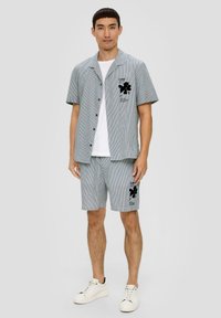 Paski, krótki rękawek, koszula i szorty, wykonane z lekkiego materiału. Posiadaj czarny graficzny wzór kwiatowy na koszuli i szortach. Białe sneakersy.