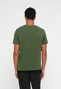 Πράσινο βαμβακερό μπλουζάκι με στρογγυλή λαιμόκοψη και κοντά μανίκια, με απλό σχέδιο και λεία υφή, που φαίνεται από πίσω.