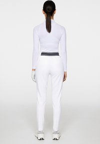 Biała bluzka z długim rękawem o dopasowanym kroju, zestawiona z dopasowanymi białymi spodniami z czarnym paskiem i jasnym obuwiem.