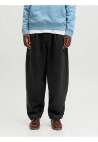 Pantalones de chándal anchos y negros, hechos de una tela suave, con cintura alta y pliegues sutiles, combinados con zapatos marrones de cordones y una sudadera azul.