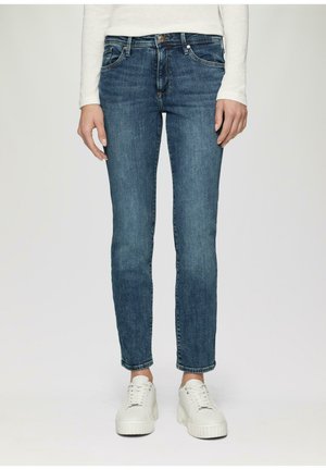 Jeans ajustados de color azul hechos de mezclilla, con cinco bolsillos, cremallera y un lavado medio. Combinados con zapatillas blancas de plataforma.