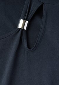 Top blu scuro realizzato in tessuto morbido, caratterizzato da un design a chiave e un accento metallico argento lucido sul colletto.