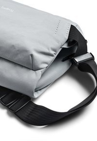 Borsa a tracolla in tessuto grigio con patta superiore imbottita, superficie texturizzata, tracolla nera regolabile e parti metalliche sulla fibbia.