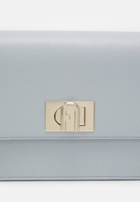 Kožená handbag modré nebe s texturovaným povrchem, zdobená zlatým kováním a geometrickým logem. Kompaktní obdélníkový tvar.