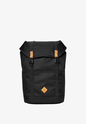 Zaino nero con patta superiore, due spallacci regolabili con fibbie e una piccola patch logo in pelle marrone chiaro al centro anteriore.