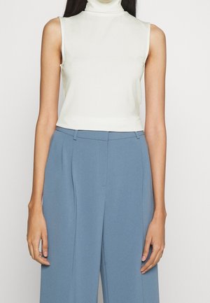 Kremowy bezrękawnik z golfem w połączeniu z jasnoniebieskimi, szerokimi spodniami z wysokim stanem. Gładki materiał z dopasowanym krojem.