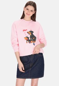 Roze sweatshirt met cartoon teckels en grafische accenten, gecombineerd met een donker denim rokje. Losse pasvorm met geribbelde boorden.