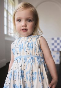 Šaty s kvetinovým vzorom, modré kvety a čierne bodky. Ľahká tkanina, bez rukávov a modrý opasok v páse. Jemná, plynulá textúra.